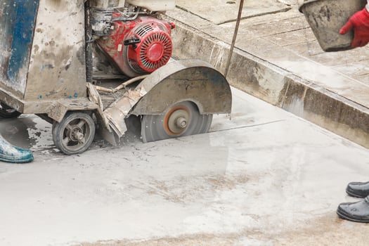 Worker using diamond saw blade machine cutting concrete road at construction site photo
