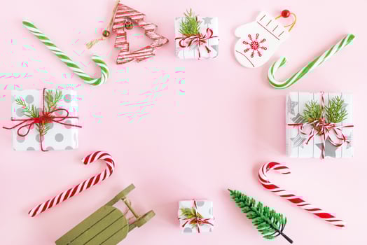 Top view on a frame from red and green wooden Christmas decorations, caramel sticks and gift boxes with fir branches on a pink background with copy space. photo