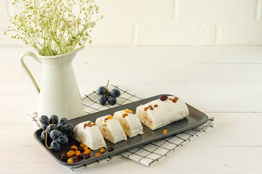 Sliced halva with nuts and dried fruits on a plate served with flowers and fruits on white table photo