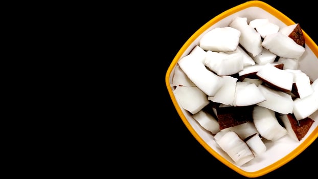 Fresh coconut pieces in a bowl on dark color background photo