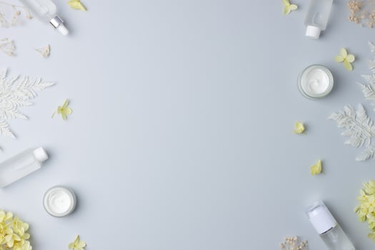 Cosmetic skin care products with with flowers on grey background. Flat lay, copy space photo