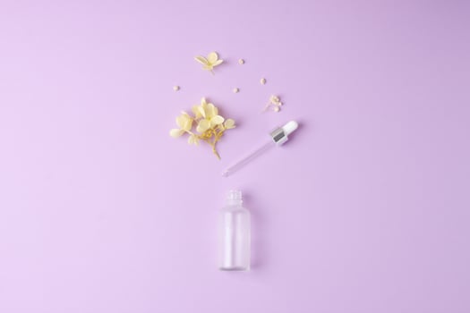 Minimal composition with cosmetic bottle with flowers on rose background. Flat lay, copy space photo