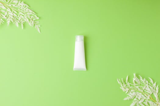 White tube of cosmetic cream with flowers on green background. Flat lay, copy space photo