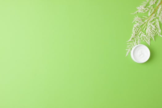 Jar of cosmetic cream with flowers on green background. Flat lay, copy space photo