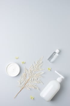 Cosmetic skin care products with flowers on grey background. Flat lay, copy space photo
