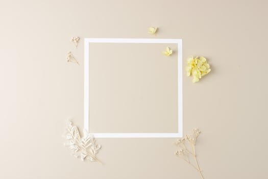 Cosmetic background with flowers and white frame on pastel beige. Flat lay, copy space photo