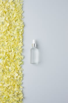 Cosmetic bottle with flowers on grey background. Flat lay, copy space photo
