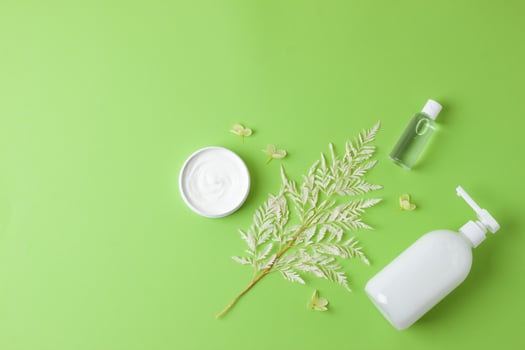 Cosmetic skin care products with flowers on green background. Flat lay, copy space photo