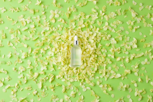 Cosmetic bottle with flowers on green background. Flat lay photo