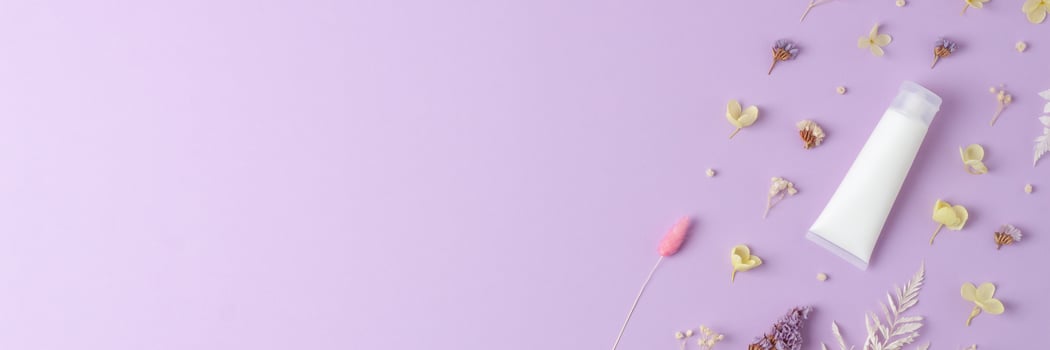 White tube of cosmetic cream with flowers on rose background. Flat lay, copy space photo