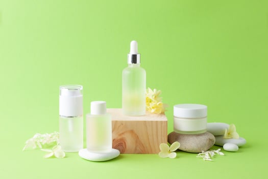 Cosmetic skin care products with wood podium and flowers, stone on green background. Close up, copy space photo
