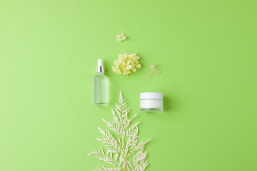 Cosmetic skin care products with flowers on green background. Flat lay, copy space photo