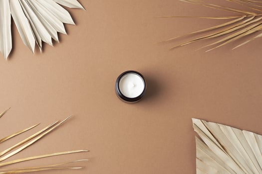 Jar of cosmetic cream with palm leaf on brown background. Flat lay photo