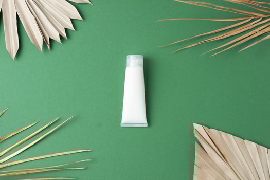 White tube of cosmetic cream with palm leaf on green background. Flat lay photo