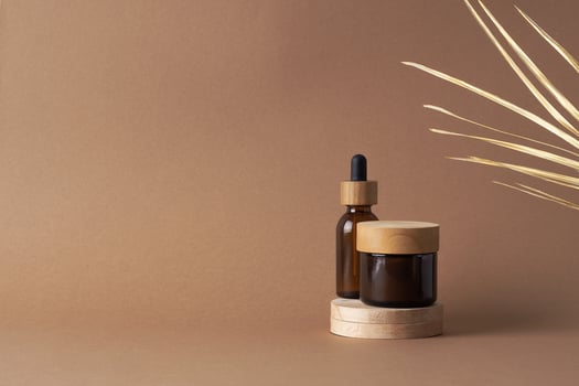 Cosmetic skin care products with wood podium and palm leaf on brown background. Close up, copy space photo