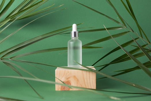 Cosmetic bottle with wood podium and palm leaf on green background. Close up, copy space photo