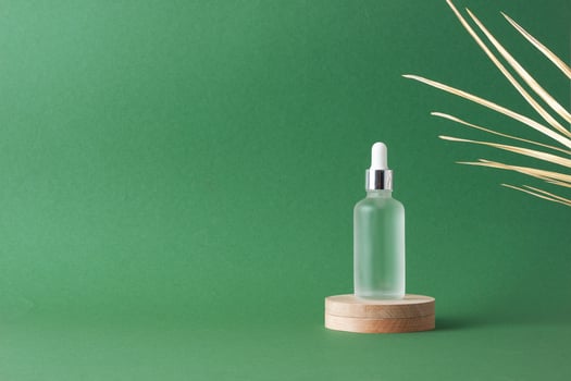Cosmetic bottle with wood podium and palm leaf on green background. Close up, copy space photo