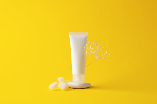 White tube of cosmetic cream on a stone podium with flowers on yellow background. Close up. photo