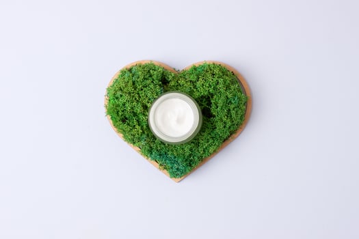 Jar of cosmetic cream with a wooden heart and moss on white background. Flat lay, copy space photo