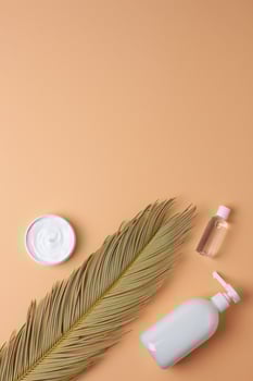Cosmetic skin care products with palm leaf on pastel beige background. Flat lay, copy space photo