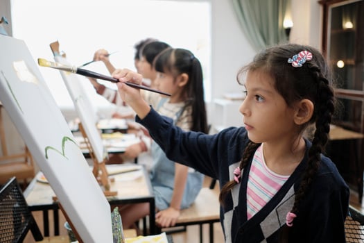 A little girl concentrates on acrylic color picture painting on canvas with multiracial kids in an art classroom, creative learning with talents and skills in the elementary school studio education. photo