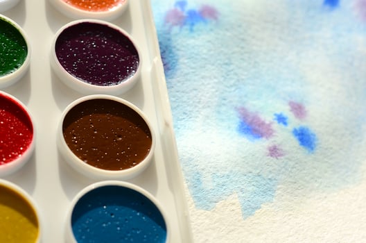 A new set of watercolors lies on a sheet of paper, which shows an abstract watercolor drawing in the form of blue strokes. The concept of amateur painting among teenagers photo