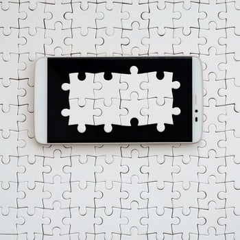 A modern big smartphone with several puzzle elements on the touch screen lies on a white jigsaw puzzle in an assembled state photo