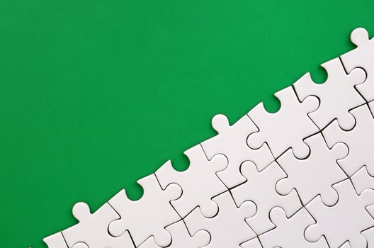 Fragment of a folded white jigsaw puzzle on the background of a green plastic surface. Texture photo with copy space for text