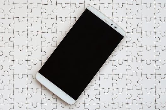 A modern big smartphone with a touch screen lies on a white jigsaw puzzle in an assembled state photo