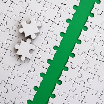 The green path is laid on the platform of a white folded jigsaw puzzle. The missing elements of the puzzle are stacked nearby. Texture image with space for text photo