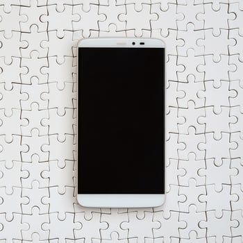 A modern big smartphone with a touch screen lies on a white jigsaw puzzle in an assembled state photo