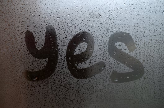 The English word Yes is written with a finger on the surface of the misted glass photo