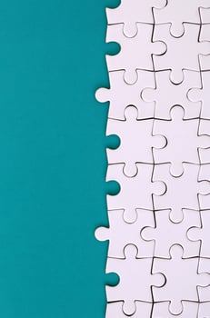 Fragment of a folded white jigsaw puzzle on the background of a blue plastic surface. Texture photo with copy space for text