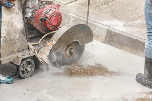 Worker using diamond saw blade machine cutting concrete road at construction site photo