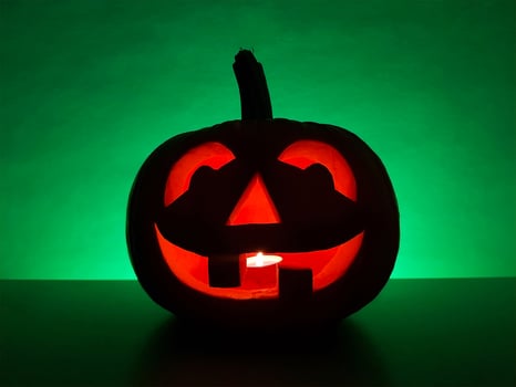Halloween carved glowing pumpkin jack-o-lantern with candle inside stands on surface in dark night and blurred defocused background. The back wall highlighted in green. Spooky holiday concept. photo