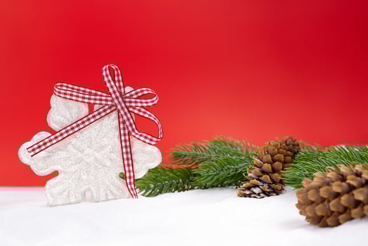 White shiny snowflake with bow, fir branches and cones on snow, red background behind. Christmas, New Year, winter. Copy space photo