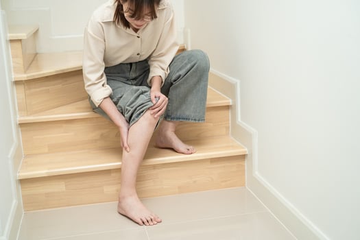 Asian lady woman touch and feel pain her knee on the stairs at home, healthy medical concept. photo