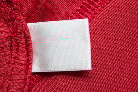 White blank laundry care clothes label on red polyester sport shirt background photo