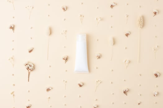 White tube of cosmetic cream with flowers on pastle beige background. Flat lay photo