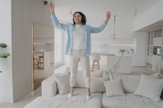 Happy energetic female in headphones celebrates success jumping on couch to music having fun at home photo