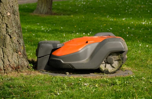Robotic Lawn Mower on green grass background.Automatic robot lawnmower in modern garden.Green grass trimming with lawn mower. Close-up view of the lawn mower dirty blade after mowing the lawn. photo