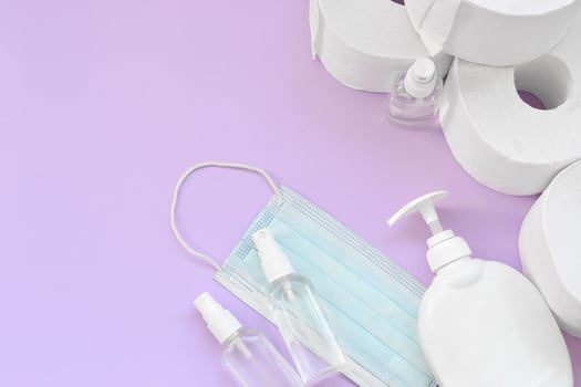 Set of important items for Covid-19 quarantine times. Toilet paper with surgical face mask and hand sanitizer with liquid soap bottle on lilac background photo