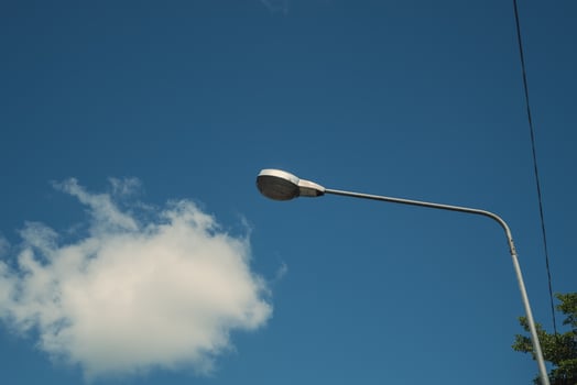 Modern electricity lamp post with blue sky and cloud as background. Steel street light or lantern on pole in the daytime are conceptualized in industrial, technological, and urbanize photo