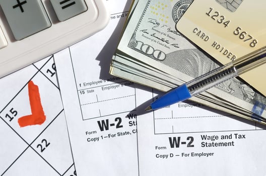 W-2 Wage and Tax statement blank with credit card on dollar bills, calculator and pen on calendar page with marked 15th April photo