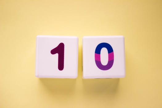 Close-up photo of a white plastic cube with a violet number 10 on a yellow background. Object in the center of the photo