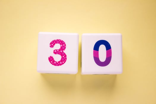 Close-up photo of a white plastic cubes with a colorful number 30 on a yellow background. Object in the center of the photo