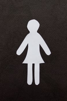 Silhouette of a woman in dress of white paper, cut by hand. In the center of vertical photo on black background