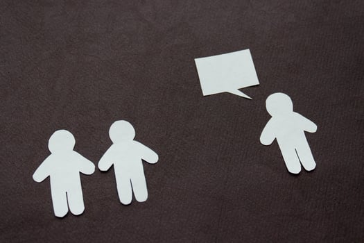 Silhouettes of people cut from white paper on a black background. A couple of people stands in front of one person who is speaking. photo