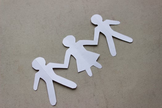 Silhouette of two man and woman between them, holding hands, cut out of white paper. In the center of the photo on a beige background