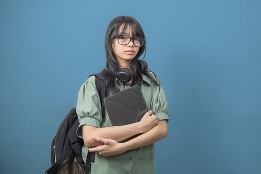 Asian woman wearing a green backpack and holding a tablet with headphones on the background. Back to school and learning concept. photo